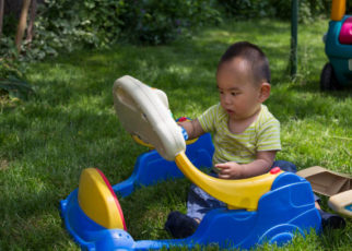 A little Chinese boy is playing toy on grassland in back yard.